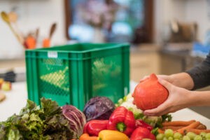 Eine Person räumt diverses Obst und Gemüse aus einer Kiste aus